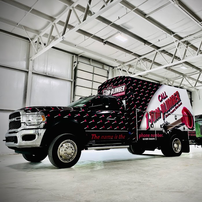 A black commercial service truck with branded vinyl wrap parked inside an industrial garage for 1-Tom-Plumber.