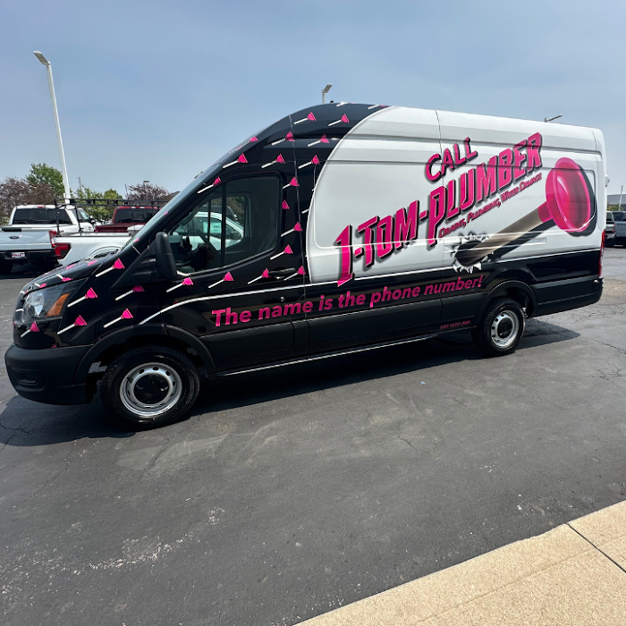 A plumbing service van with company wrap and contact details parked on an asphalt parking lot for 1-Tom-Plumber.